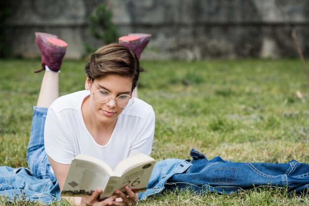 Concentrated young woman reading lying on lawn