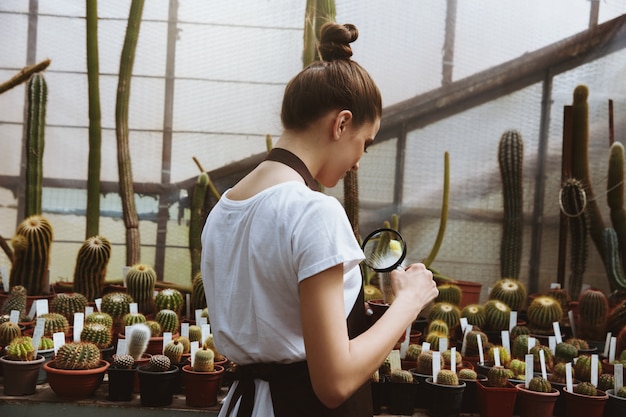 Concentrated young woman standing in greenhouse near plants