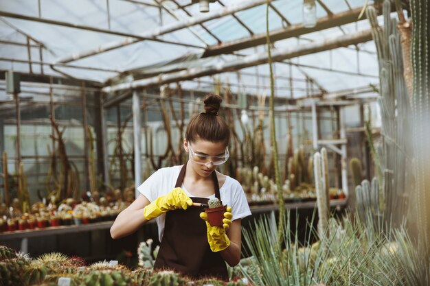 Concentrated young woman standing in greenhouse near plants