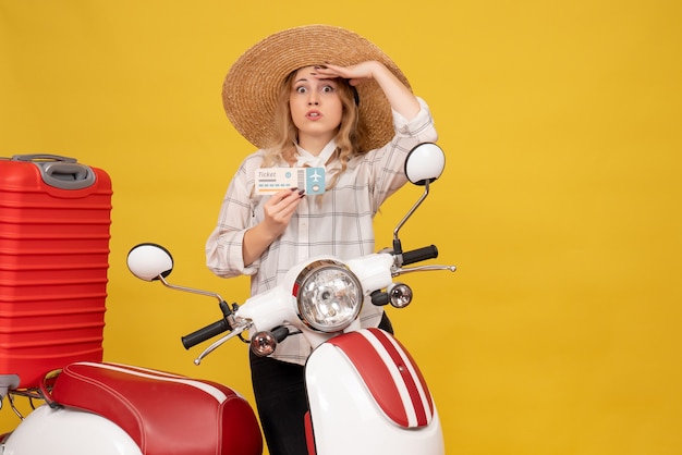 Сосредоточенная молодая женщина в шляпе собирает свой багаж, сидит на мотоцикле и показывает билет, внимательно глядя на что-то