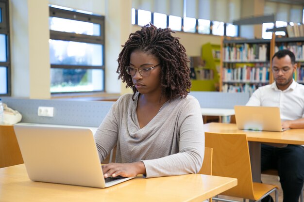 Concentrated young woman working with laptop at library