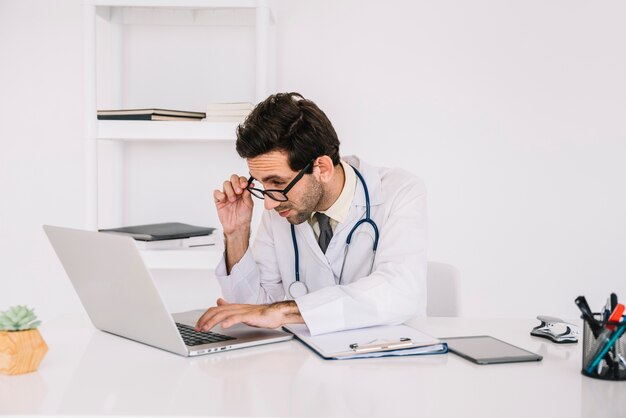Concentrating young male doctor working on laptop in clinic