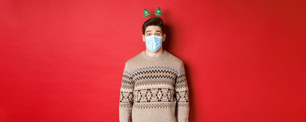 クリスマスcovidと社会的距離の陽気な若い男の医療マスクと新年のクロの概念