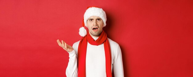 Концепция рождественских зимних праздников и праздничного портрета растерянного мужчины в новогодней шапке и шарфе...