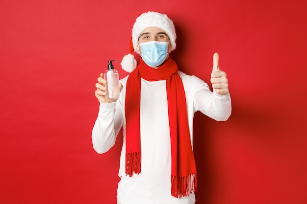 Concept of covid christmas and holidays during pandemic happy and satisfied man in santa hat and med...