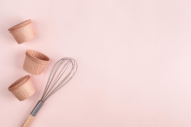 The concept of homemade baking is a whisk for whipping and cupcake molds on a pink background. Zero waste. Copy space. Top view. Baking concept. flat lay
