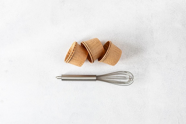 The concept of homemade baking is a whisk for whipping and cupcake molds on a white background Zero waste Copy space Top view