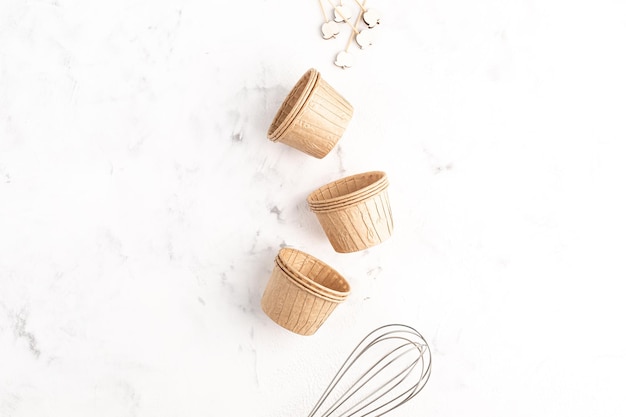 The concept of homemade cakes A whisk and paper cupcake molds on a white stone background Recipe for muffins with apples Zero waste Copy space Top view Baking concept flat lay
