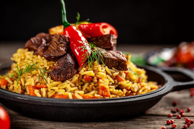 The concept of oriental cuisine. national uzbek pilaf with meat in a cast-iron skillet, on a wooden table. background image. top view, copy space, flat lay