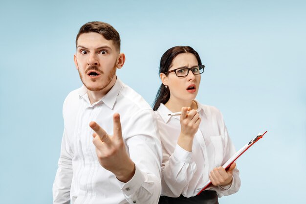 Concept of partnership in business. Young emotional man and woman against blue background at studio. Human emotions and partnership concept