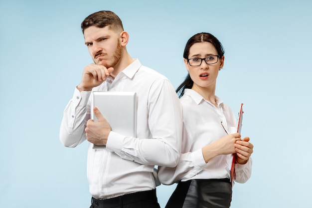 Concept of partnership in business. Young man and woman looking suspicious against blue background at studio