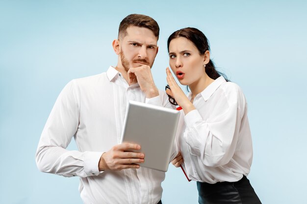 Concept of partnership in business. Young man and woman looking suspicious against blue wall