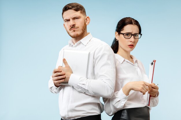 Concept of partnership in business. Young man and woman looking suspicious against blue wall