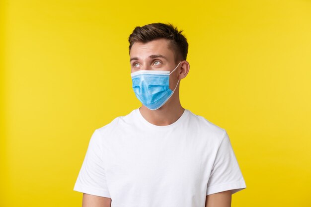 Concept of social distancing, covid-19 and people emotions. Close-up portrait of blond guy in medical mask turn face and look upper left corner with unbothered careless expression.