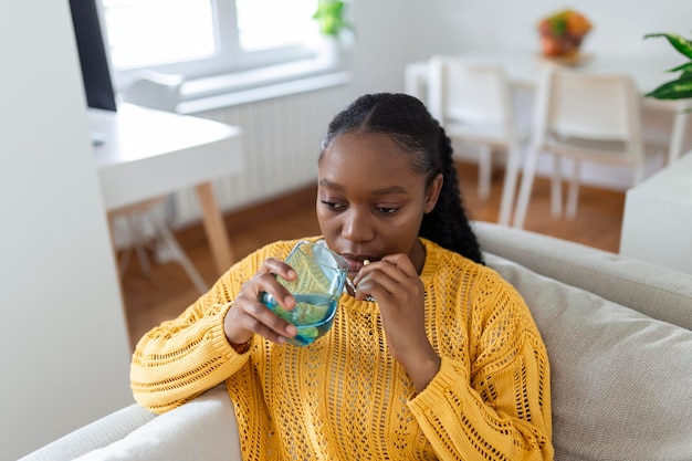 Concept of suffering from terrible pain Beautiful sad upset unhappy troubled weak woman with black hair wearing casual clothes is sitting on a sofa and taking a pill