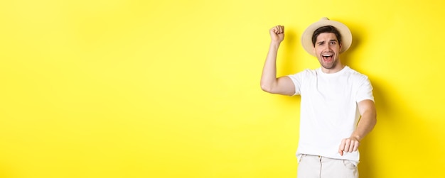 Concept of tourism and summer young man traveller showing rodeo gesture standing in straw hat and wh