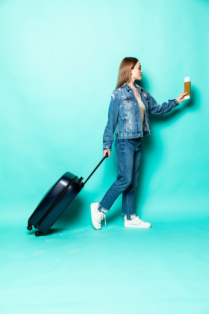 Concept of travel. Happy woman girl with suitcase and passport on green colored wall