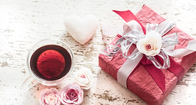 The concept of Valentine's Day and Mother's Day, a red gift box with a bow with roses and a cup of tea on a light wooden background