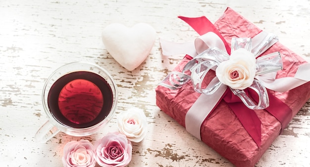 バレンタインデーと母の日、バラの弓と軽い木製の背景にお茶のカップの赤いギフトボックスの概念