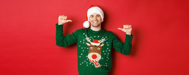 Концепция зимних праздников, рождества и образа жизни счастливый привлекательный парень в шляпе Санты и свитере с капюшоном...