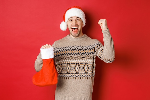 Concept of winter holidays, new year and celebration. Amazed and happy man shouting for joy, found gift inside christmas stocking and cheering, raising hand up and smiling