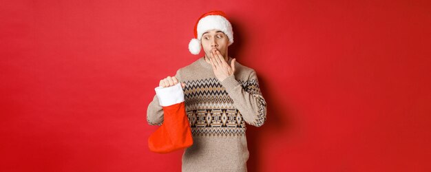 Concept of winter holidays new year and celebration surprised adult man holding christmas stocking w...