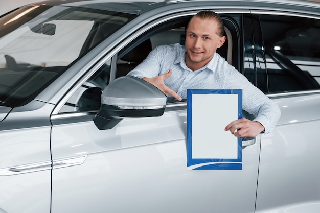Бесплатное фото Концепция бизнеса. менеджер сидит в современной белой машине с бумагой и документами в руках