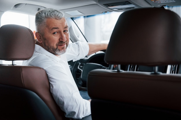 Conception of success. Joyful bearded man in white shirt looks back while sitting in the modern car