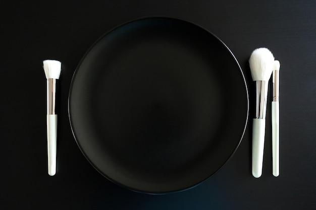 Free photo conceptual image of make up brushes next to dinner plate on black background