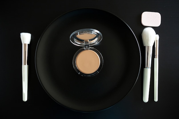 Conceptual image of make up brushes next to dinner plate on black background