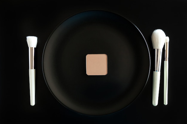 Conceptual image of make up brushes next to dinner plate on black background