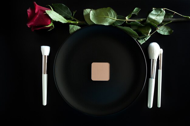 Conceptual image of make up brushes next to dinner plate on black background