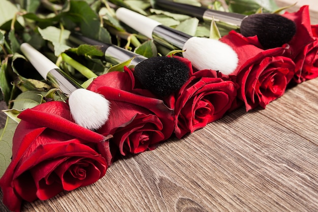 Conceptual image of make-up brushes next to roses on wooden background