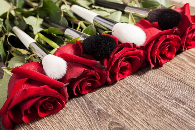 Концептуальное изображение кистей для макияжа рядом с розами на деревянных фоне