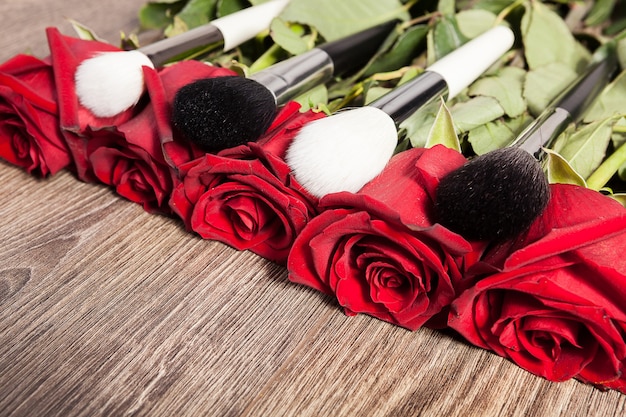 Conceptual image of make-up brushes next to roses on wooden background