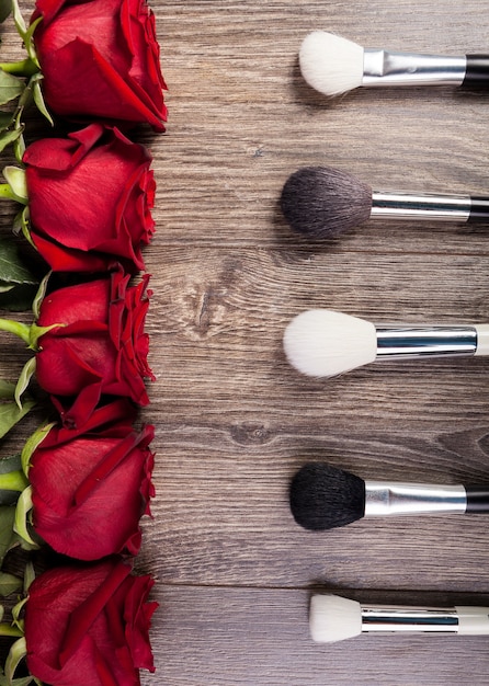 Conceptual image of make-up brushes next to roses on wooden background