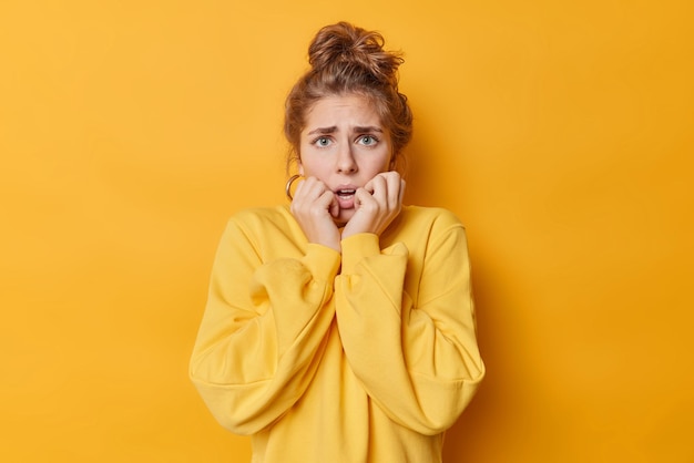 Concerned anxious european woman trembles from fright grabs face stands shocked indoor notices something horrified dressed in jumper isolated over yellow background. human reactions concept