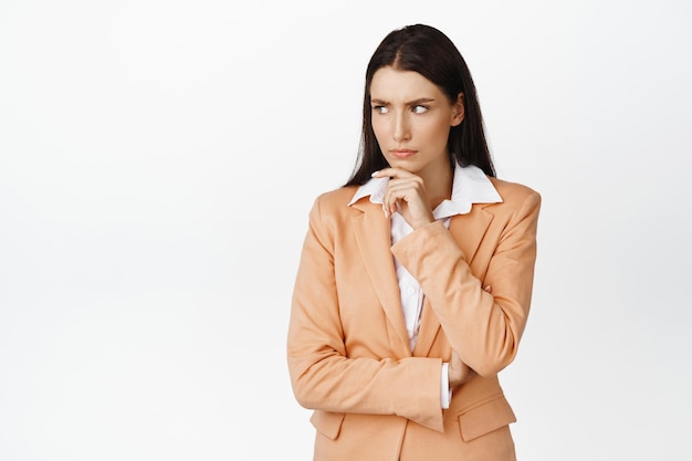 Concerned corporate woman thinking looking aside with troubled thoughtful expression solving problem in her head standing in suit over white background