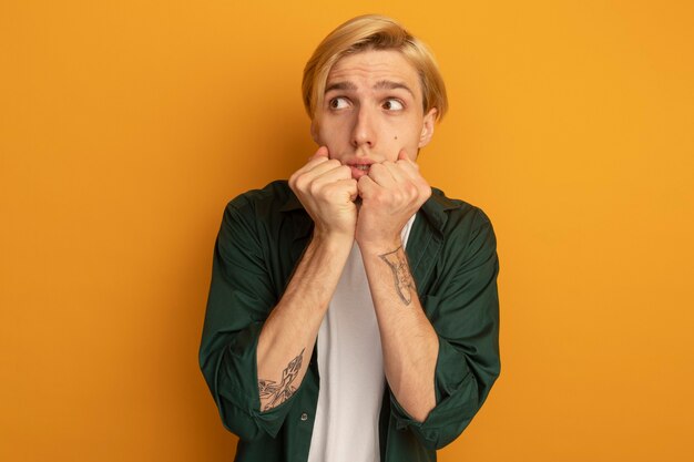 Concerned looking at side young blonde guy wearing green t-shirt putting hands under chin