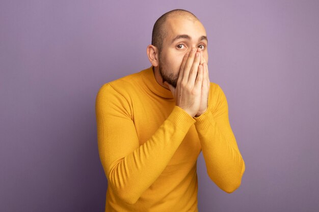 Concerned looking straight ahead young handsome guy covered face with hands isolated on purple