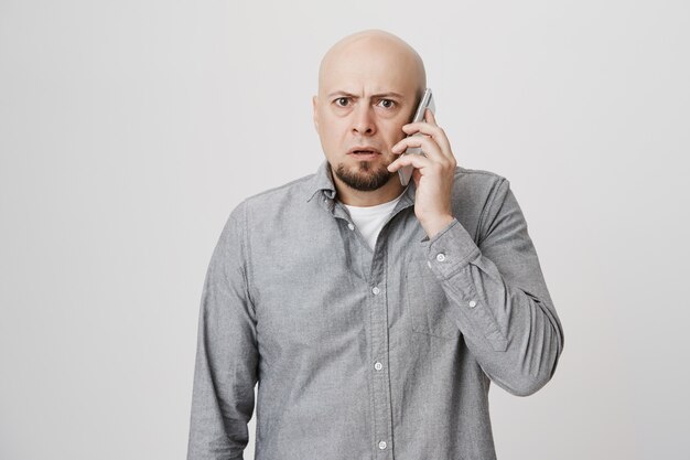 Concerned middle-aged bald man having phone conversation