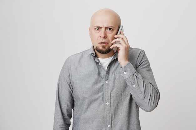 Обеспокоенный лысый мужчина средних лет разговаривает по телефону