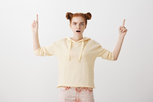 Concerned shocked redhead girl pointing fingers up