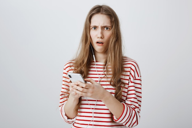 Обеспокоенная и шокированная женщина обеспокоенно смотрит после прочтения странного сообщения на мобильном телефоне