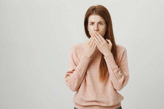 Concerned teenage redhead girl shut mouth and look worried