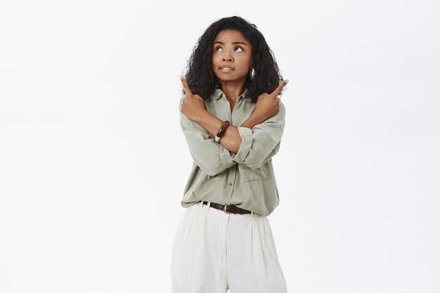 Concerned troubled attractive african american adult woman with curly hairstyle feeling unsure crossing arms on body and pointing in different directions