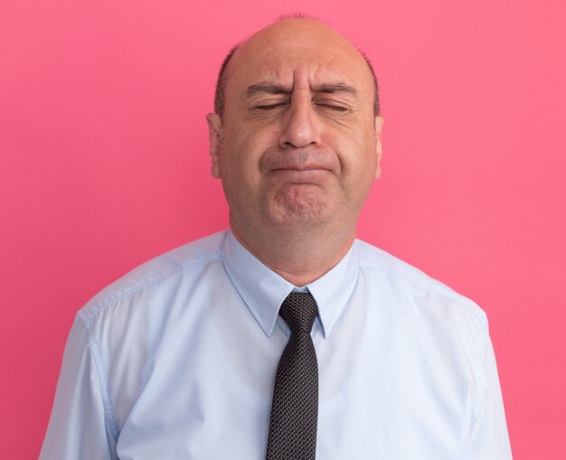 Concerned with closed eyes middle-aged man wearing white t-shirt with tie isolated on pink wall