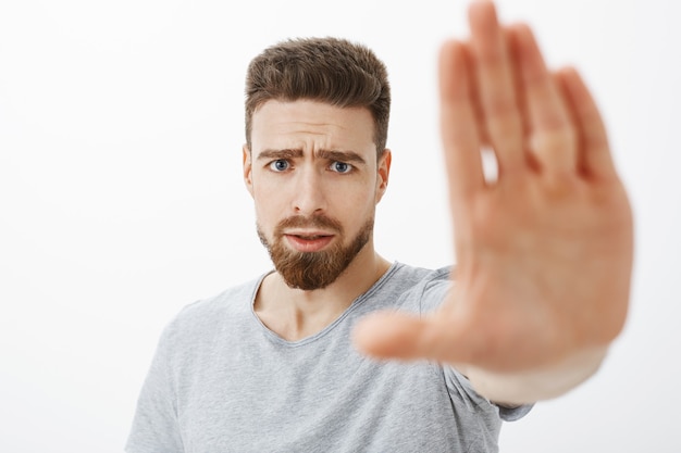 Free photo concerned and worried handsome young male friend with blue eyes, beard and moustache pulling palm towards to warn and stop from making bad choices frowning looking anxious worrying for mate