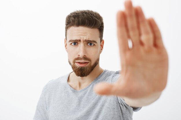 Concerned and worried handsome young male friend with blue eyes, beard and moustache pulling palm towards to warn and stop from making bad choices frowning looking anxious worrying for mate