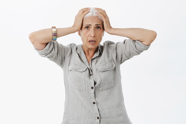 Concerned and worried senior woman panicking, grab head and looking distressed